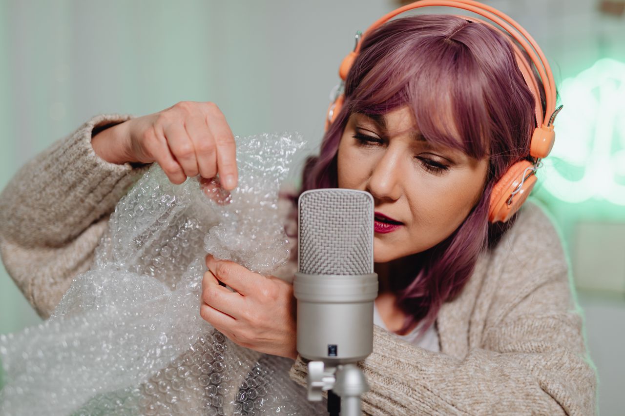 A woman creating ASMR sounds with bubble wrap, enhancing relaxation through a microphone.