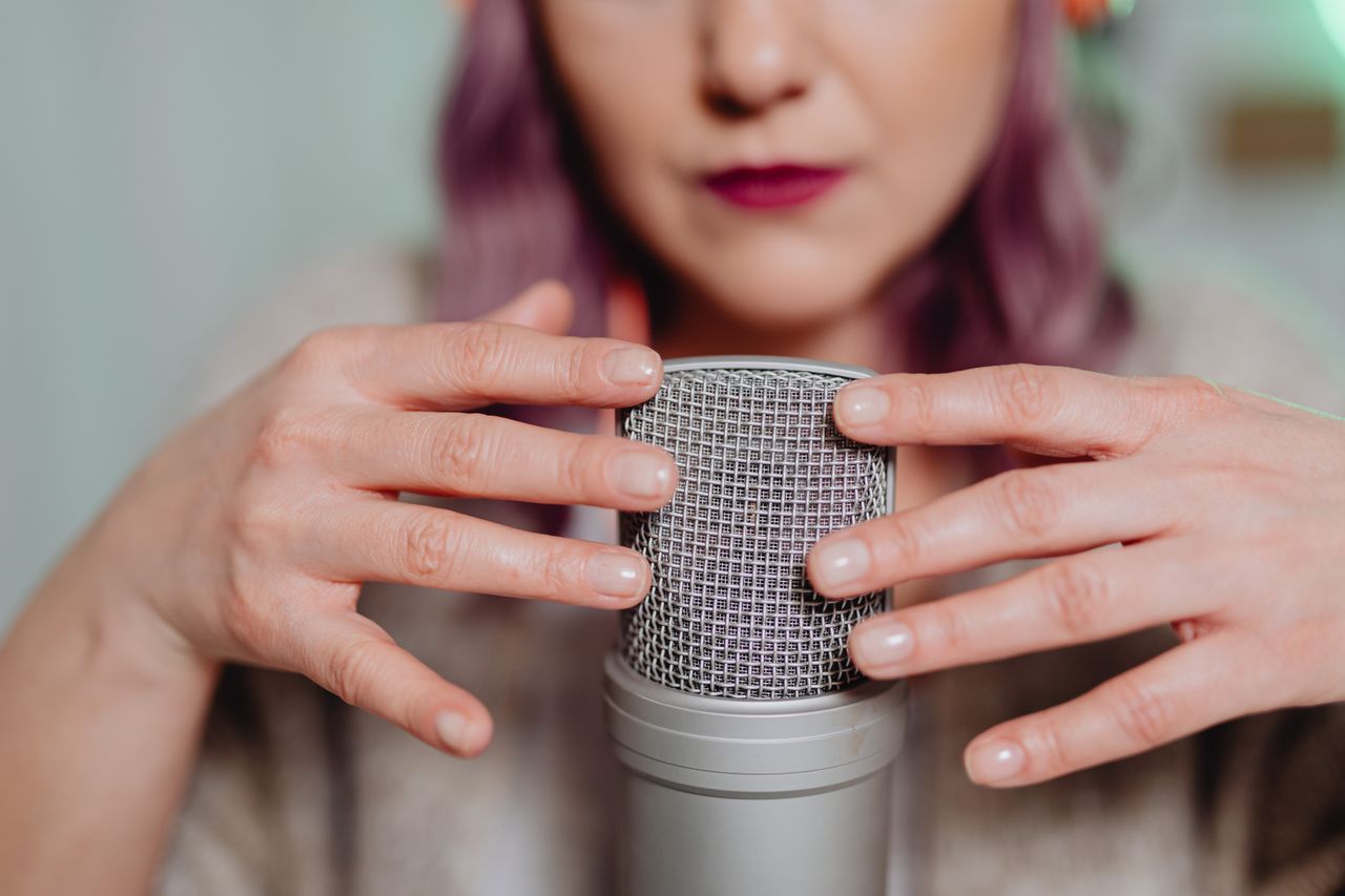 About Woman using a microphone for ASMR recording indoors, creating soothing audio.