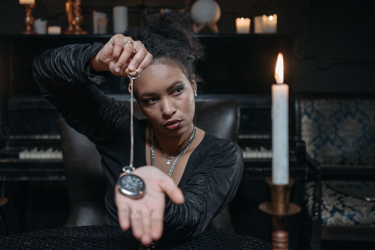 Portrait of a woman performing hypnosis with a pocket watch in a candlelit room.